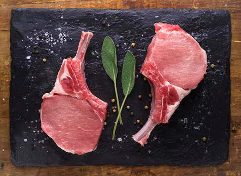 Bone-in pork chops over a piece of stone slate and wooden background